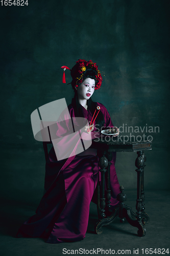 Image of Young japanese woman as geisha on dark green background. Retro style, comparison of eras concept.