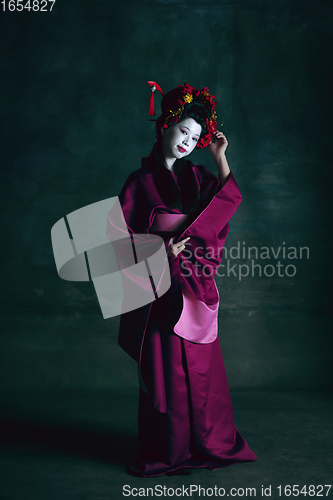 Image of Young japanese woman as geisha on dark green background. Retro style, comparison of eras concept.