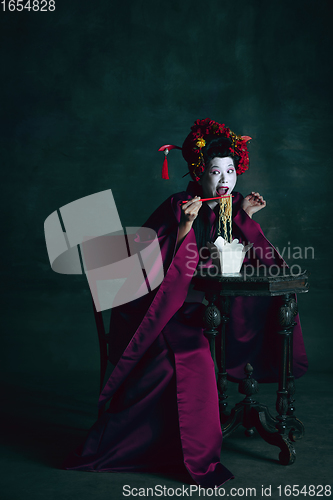 Image of Young japanese woman as geisha on dark green background. Retro style, comparison of eras concept.