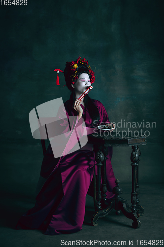 Image of Young japanese woman as geisha on dark green background. Retro style, comparison of eras concept.