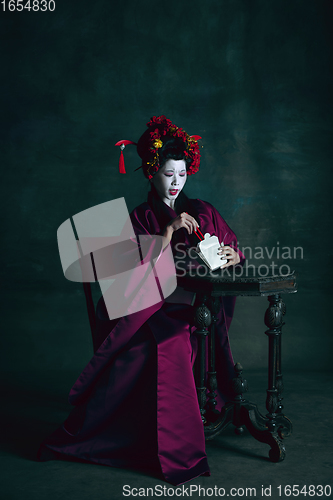 Image of Young japanese woman as geisha on dark green background. Retro style, comparison of eras concept.