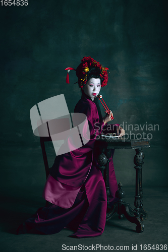 Image of Young japanese woman as geisha on dark green background. Retro style, comparison of eras concept.