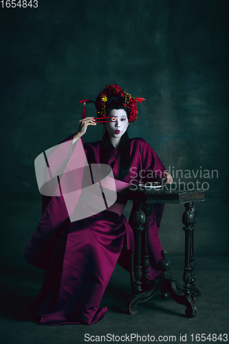 Image of Young japanese woman as geisha on dark green background. Retro style, comparison of eras concept.