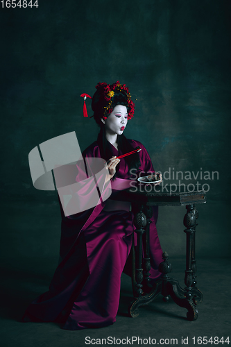 Image of Young japanese woman as geisha on dark green background. Retro style, comparison of eras concept.