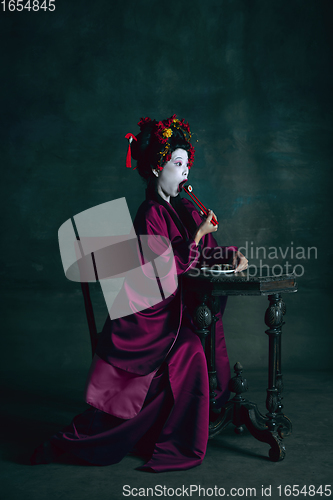 Image of Young japanese woman as geisha on dark green background. Retro style, comparison of eras concept.