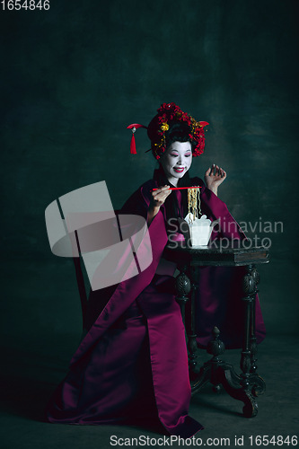 Image of Young japanese woman as geisha on dark green background. Retro style, comparison of eras concept.