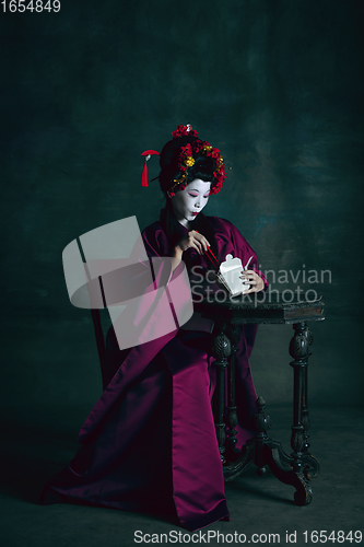 Image of Young japanese woman as geisha on dark green background. Retro style, comparison of eras concept.