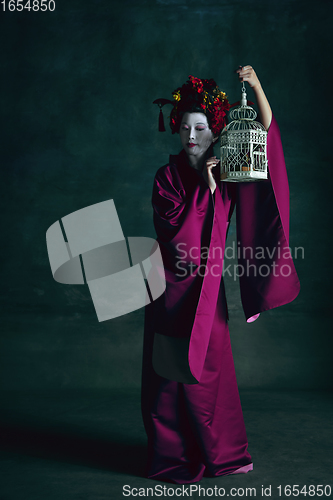 Image of Young japanese woman as geisha on dark green background. Retro style, comparison of eras concept.