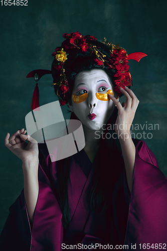 Image of Young japanese woman as geisha on dark green background. Retro style, comparison of eras concept.