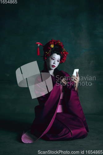 Image of Young japanese woman as geisha on dark green background. Retro style, comparison of eras concept.