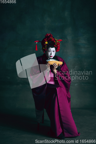 Image of Young japanese woman as geisha on dark green background. Retro style, comparison of eras concept.