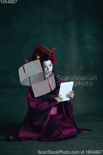 Image of Young japanese woman as geisha on dark green background. Retro style, comparison of eras concept.