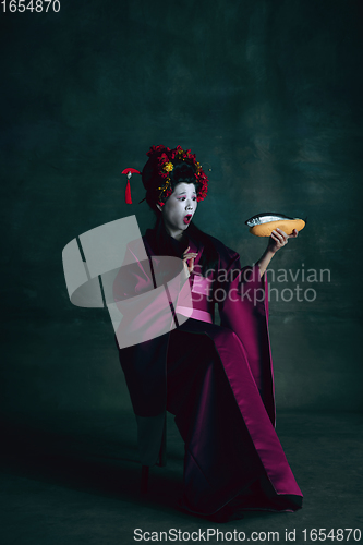 Image of Young japanese woman as geisha on dark green background. Retro style, comparison of eras concept.