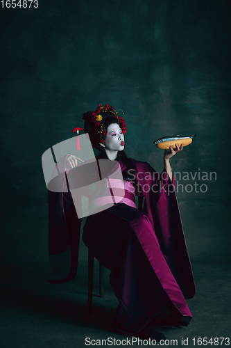 Image of Young japanese woman as geisha on dark green background. Retro style, comparison of eras concept.