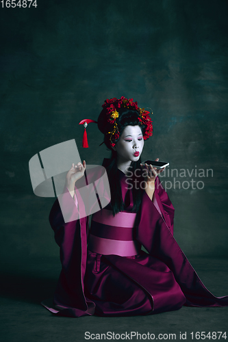 Image of Young japanese woman as geisha on dark green background. Retro style, comparison of eras concept.