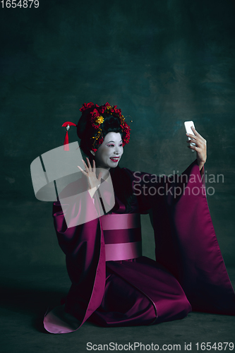 Image of Young japanese woman as geisha on dark green background. Retro style, comparison of eras concept.