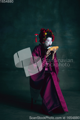 Image of Young japanese woman as geisha on dark green background. Retro style, comparison of eras concept.