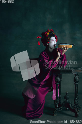 Image of Young japanese woman as geisha on dark green background. Retro style, comparison of eras concept.