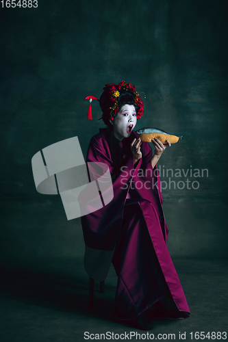 Image of Young japanese woman as geisha on dark green background. Retro style, comparison of eras concept.