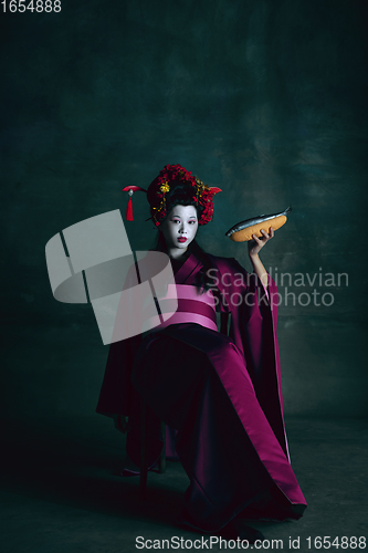 Image of Young japanese woman as geisha on dark green background. Retro style, comparison of eras concept.