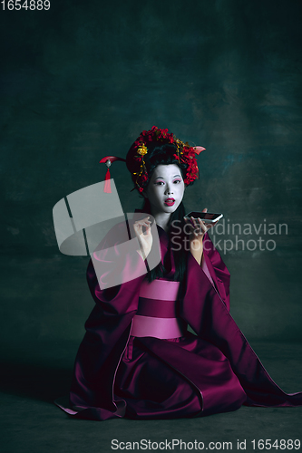 Image of Young japanese woman as geisha on dark green background. Retro style, comparison of eras concept.