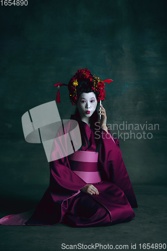 Image of Young japanese woman as geisha on dark green background. Retro style, comparison of eras concept.