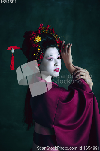 Image of Young japanese woman as geisha on dark green background. Retro style, comparison of eras concept.