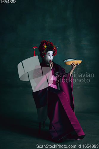 Image of Young japanese woman as geisha on dark green background. Retro style, comparison of eras concept.