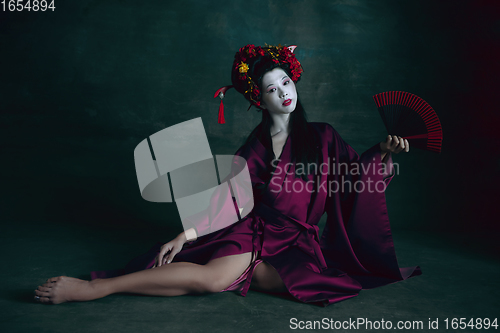 Image of Young japanese woman as geisha on dark green background. Retro style, comparison of eras concept.