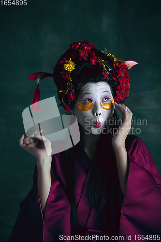 Image of Young japanese woman as geisha on dark green background. Retro style, comparison of eras concept.