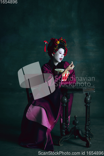 Image of Young japanese woman as geisha on dark green background. Retro style, comparison of eras concept.