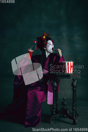 Image of Young japanese woman as geisha on dark green background. Retro style, comparison of eras concept.