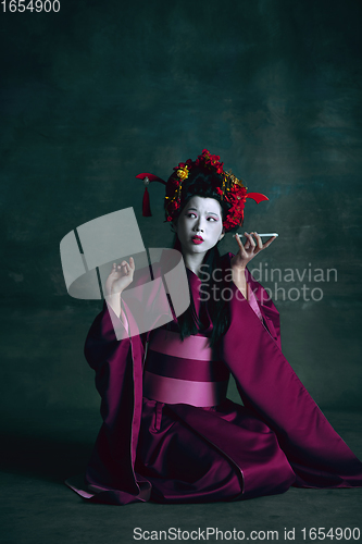 Image of Young japanese woman as geisha on dark green background. Retro style, comparison of eras concept.