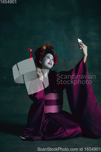 Image of Young japanese woman as geisha on dark green background. Retro style, comparison of eras concept.