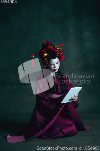 Image of Young japanese woman as geisha on dark green background. Retro style, comparison of eras concept.