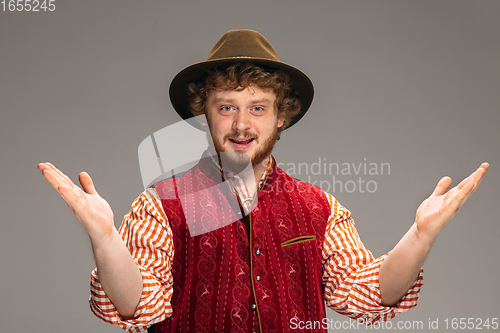 Image of Happy smiling man dressed in traditional Austrian or Bavarian costume gesturing isolated on grey studio background