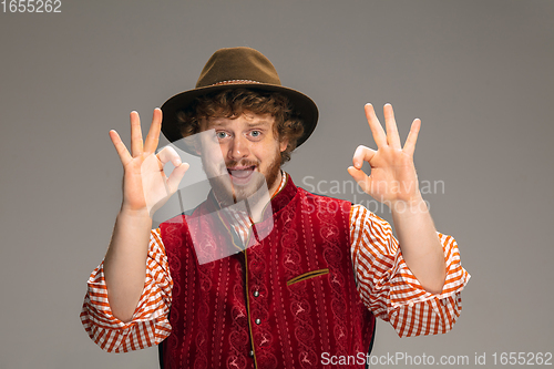 Image of Happy smiling man dressed in traditional Austrian or Bavarian costume gesturing isolated on grey studio background