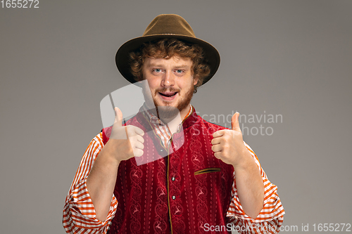 Image of Happy smiling man dressed in traditional Austrian or Bavarian costume gesturing isolated on grey studio background