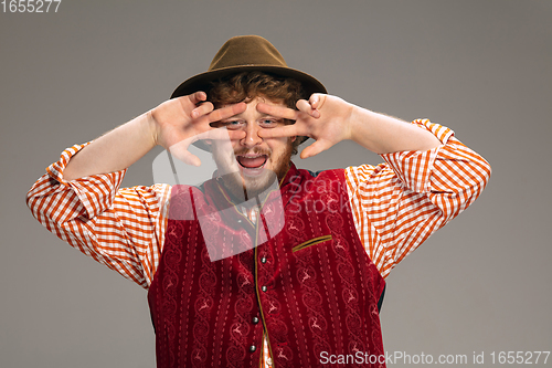 Image of Happy smiling man dressed in traditional Austrian or Bavarian costume gesturing isolated on grey studio background