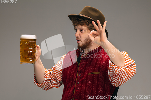 Image of Happy smiling man dressed in traditional Austrian or Bavarian costume gesturing isolated on grey studio background