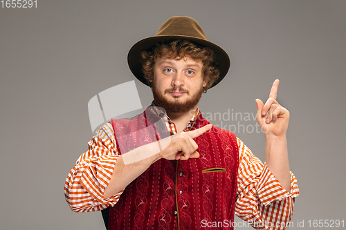 Image of Happy smiling man dressed in traditional Austrian or Bavarian costume gesturing isolated on grey studio background