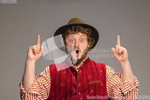 Image of Happy smiling man dressed in traditional Austrian or Bavarian costume gesturing isolated on grey studio background