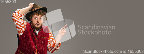 Image of Happy smiling man dressed in traditional Austrian or Bavarian costume gesturing isolated on grey studio background