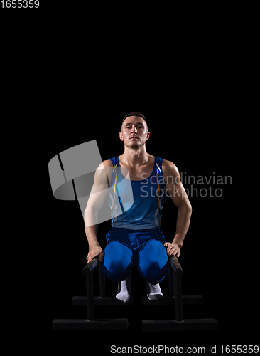 Image of Muscular male gymnast training in gym, flexible and active. Caucasian fit guy, athlete in blue sportswear isolated on black