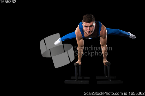 Image of Muscular male gymnast training in gym, flexible and active. Caucasian fit guy, athlete in blue sportswear isolated on black