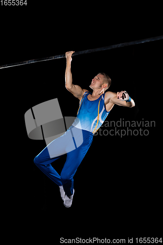 Image of Muscular male gymnast training in gym, flexible and active. Caucasian fit guy, athlete in blue sportswear isolated on black