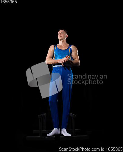 Image of Muscular male gymnast training in gym, flexible and active. Caucasian fit guy, athlete in blue sportswear isolated on black