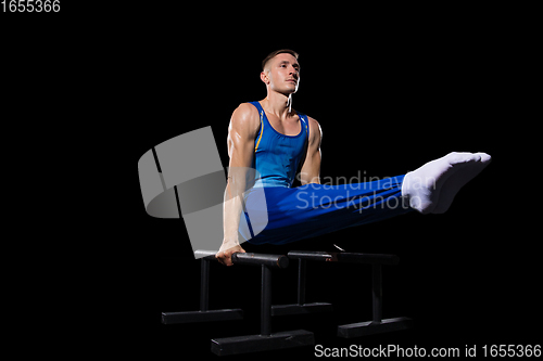 Image of Muscular male gymnast training in gym, flexible and active. Caucasian fit guy, athlete in blue sportswear isolated on black