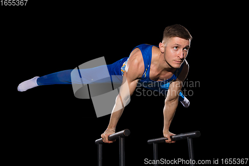 Image of Muscular male gymnast training in gym, flexible and active. Caucasian fit guy, athlete in blue sportswear isolated on black