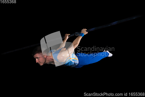 Image of Muscular male gymnast training in gym, flexible and active. Caucasian fit guy, athlete in blue sportswear isolated on black